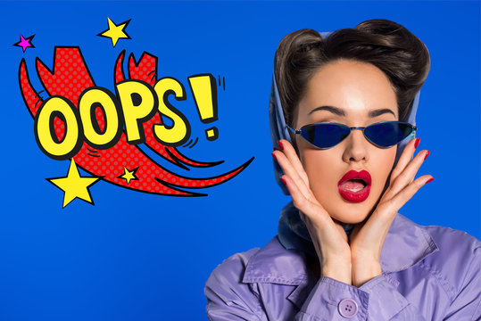 portrait of stylish woman in retro clothing and sunglasses with comic style oops sign isolated on blue - Powered by Adobe