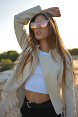 estilosa y atractiva mujer joven o chica de pelo largo y rubio con gafas de sol de colores en un parque de la ciudad durante el atardecer