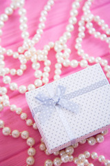 White gift box surrounded by pearl necklace on pink wooden background