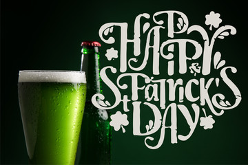 close up view of bottle and glass of beer with happy st patricks day lettering on green background