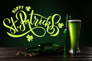 close up view of glass of beer and bottles on wooden tabletop with happy st patricks lettering