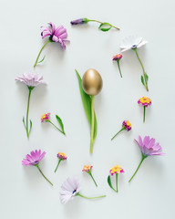 Easter egg layout made of colorful flowers ,green leaves and golden egg. Minimal easter concept. Flat lay.