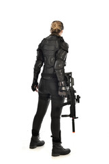 full length portrait of female  soldier wearing black  tactical armour, standing  with back to the camera holding a gun, isolated on white studio background.