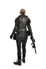 full length portrait of female  soldier wearing black  tactical armour, standing  with back to the camera holding a gun, isolated on white studio background.