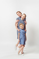 smiling mother and daughters in similar dresses isolated on grey