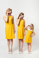 stylish mother and daughters in similar retro style yellow dresses looking at each other on white