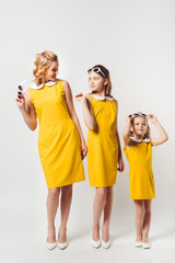 stylish mother and daughters in similar retro style yellow dresses on white
