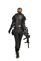 full length portrait of female  soldier wearing black  tactical armour, standing  with back to the camera holding a gun, isolated on white studio background.