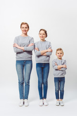 Fototapeta premium smiling mother and daughters of different generations in similar clothing with arms crossed isolated on grey
