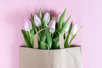 Fresh pink tulips flowers in paper bag on pink background. Top view with copy space. Flat lay.