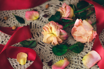 limp roses with red ribbon on a white lace doily in vintage style