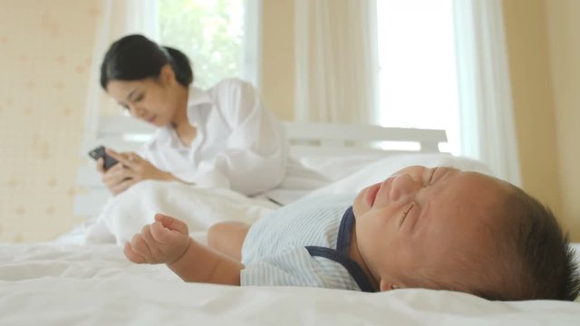 Young cell phone addict mother using smartphone for chatting on bed and leave her new born child crying. internet addiction and mobile abuse concept.