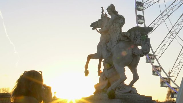 Female tourist taking photo of Pegasus Equestrian statue and Big Wheel, sunset