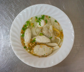 A bowl of noodle with variety of fish balls in Thai style on stainless steel table.