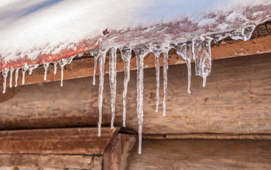 Icy icicles under the roof of wooden house