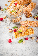 Healthy breakfast and snack concept, homemade granola with fresh raspberries in jar and nuts and granola bars, on grey stone stone background copy space