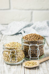 Brown and green buckwheat in glass jars on white wooden background. Selective focus, copy space. 