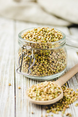 Green buckwheat in glass jars on white wooden background. Selective focus, copy space.