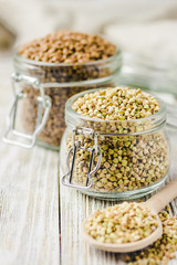 Brown and green buckwheat in glass jars on white wooden background. Selective focus, copy space. 