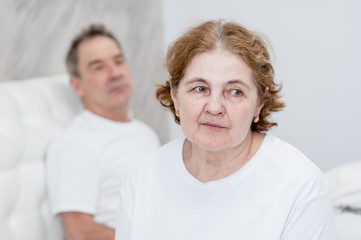 Upset senior couple sitting on bed at home