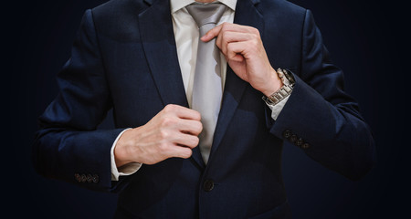 Young businessman in blue suit touching necktie, on dark blue background