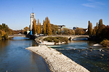 Beautiful autumnal view of the blue waters of Isar river in Munich, with the tower of the Deutsches...