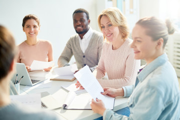 Group of confident colleagues looking at co-worker while he making report at meeting