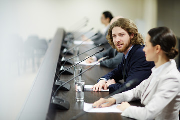 Young politician in suit talking to speaker or commenting report at conference