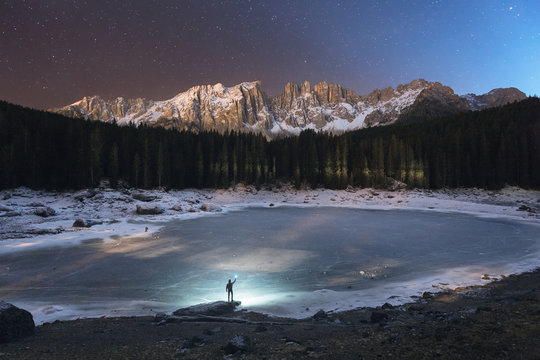 Silhouette of man standing near frozen lake at night