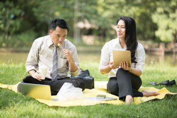 Selective focus business couple relaxing with tablets in park after work done