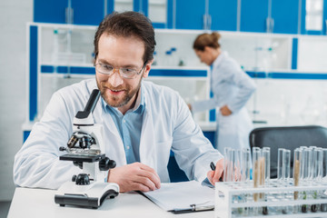 Naklejka na ściany i meble selective focus of scientist in white coat and eyeglasses at workplace with microscope in laboratory