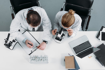 overhead view of scientific researchers in white coats working together at workplace in laboratory