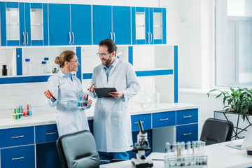 scientific researchers in white coats and eyeglasses with flasks and notepad in laboratory