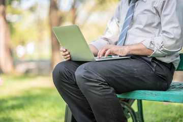 Businessman sitting on the park bench with laptop on his lap and checking the email.