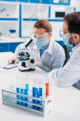 selective focus of tubes with reagents and scientists at workplace in lab