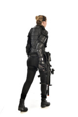 full length portrait of female  soldier wearing black  tactical armour, standing  with back to the camera holding a gun, isolated on white studio background.