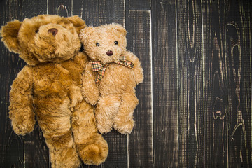 Close up top view of two hugging cute soft brown teddy bears laying together on wooden shabby background with copy space at right side. Horizontal color photography.