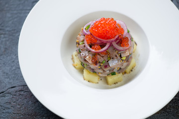 Herring fillet tartare on a bed of potato with red caviar topping served in a white plate, closeup, selective focus