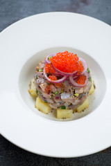 Close-up of a white plate with herring tartare, vertical shot, selective focus
