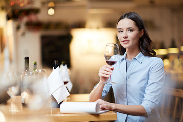 Female sommelier tasting wine at restaurant. She chooses the best wine and writing it in her notepad
