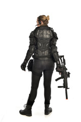 full length portrait of female  soldier wearing black  tactical armour, standing  with back to the camera holding a gun, isolated on white studio background.