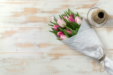 Pink tulips wrapped in white paper on wooden background. Flat lay. Love concept.