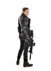 full length portrait of female  soldier wearing black  tactical armour, standing  with back to the camera holding a gun, isolated on white studio background. © faestock