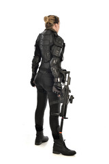 full length portrait of female  soldier wearing black  tactical armour, standing  with back to the camera holding a gun, isolated on white studio background.