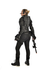 Naklejka premium full length portrait of female soldier wearing black tactical armour, standing with back to the camera holding a gun, isolated on white studio background.