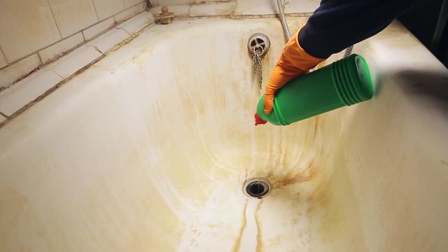 Male hand in orange rubber gloves pours a gel into the sink to clean or wash the tub and toilet in the bathroom. General house cleaning.