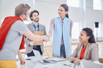 Young successful colleagues handshaking over workplace after negotiation or presentation