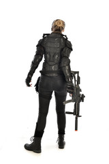 full length portrait of female  soldier wearing black  tactical armour, standing  with back to the camera holding a gun, isolated on white studio background.