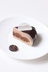 Piece of Contemporary Mousse Cake covered with Chocolate Glaze and White Velvet Spray, on white plate, on white background.