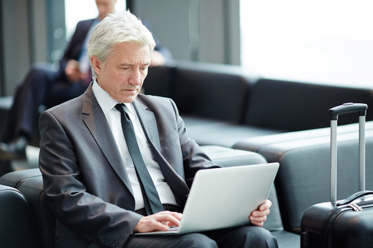 Senior businessman sitting in airport lounge with laptop in front and browsing in the net